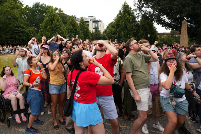 Jenny Mandl (center left in red) and Carl Endrulat (center right in red) lead a group of about 1,000 people in eating apples at Meridian Hill Park on August 15, 2026.